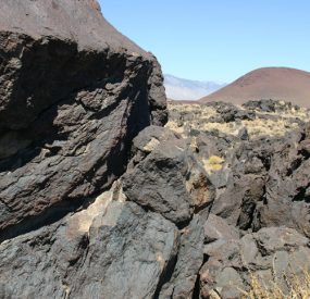 cooled lava formations with a red cinder cone in the background